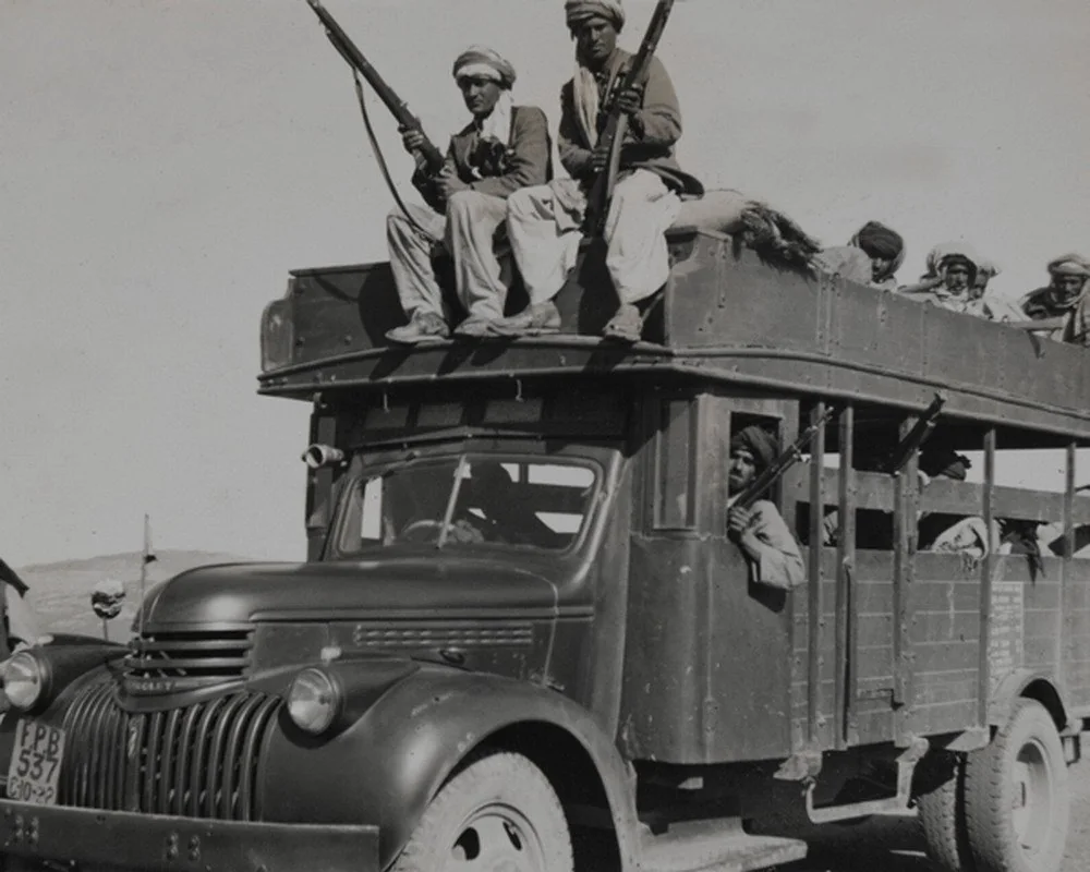 A 1947 black and white photograph of armed tribesmen standing on and around a truck during the first Kashmir war.